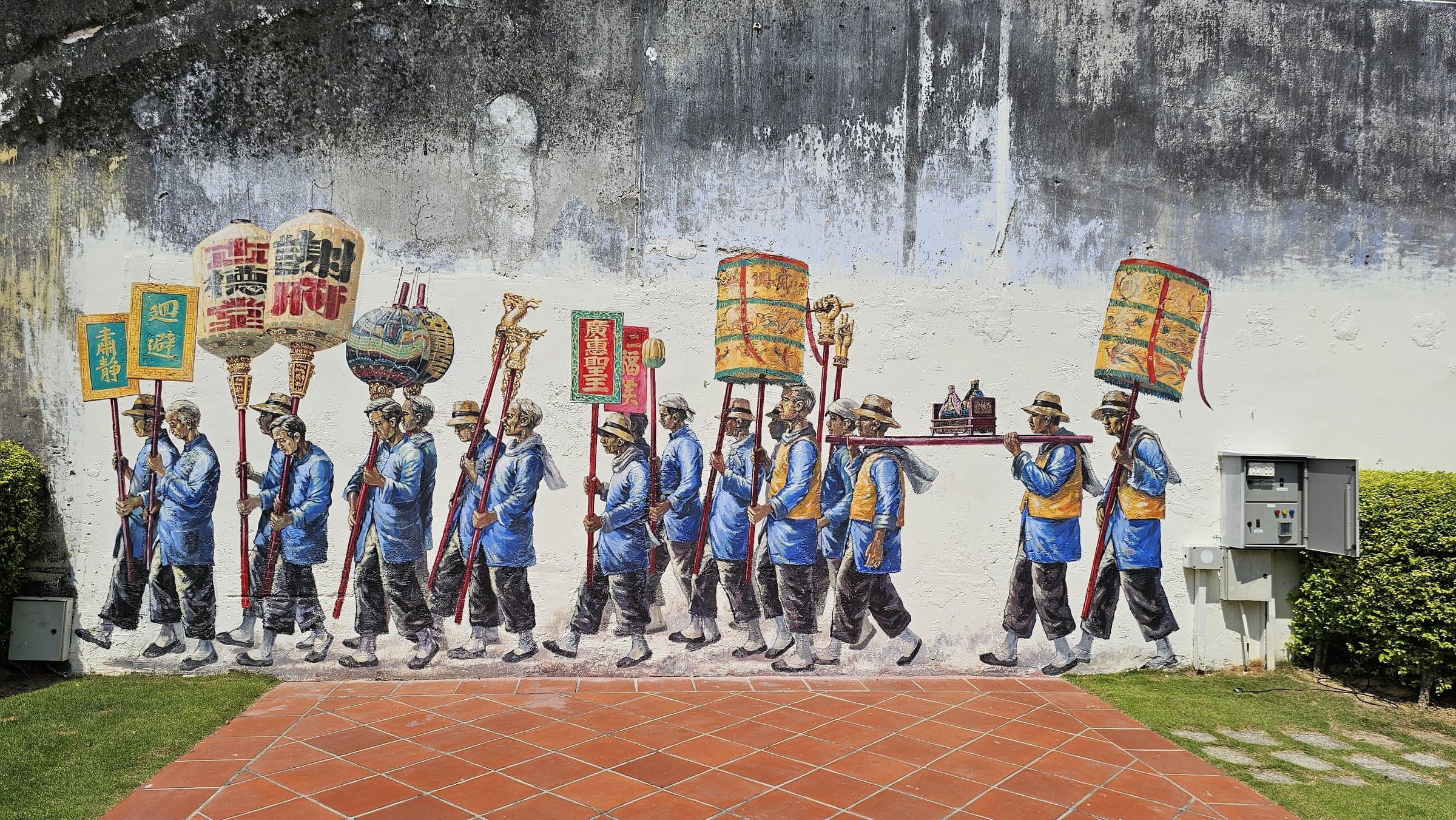 A weathered street mural in George Town showing a painted Chinese funeral procession carrying colourful paper effigies and lanterns